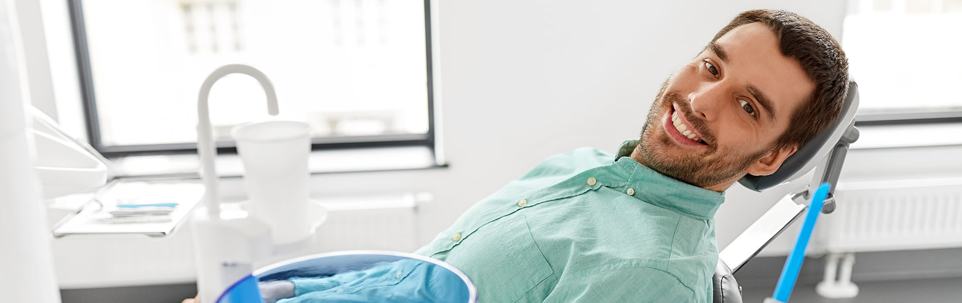 A person is seated in a dental chair, receiving care from a dental professional who stands behind them.