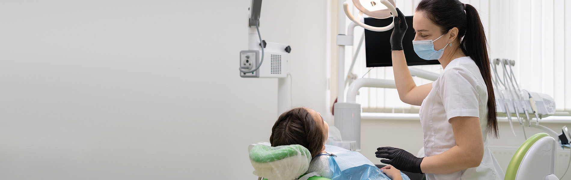 A dental hygienist in a mask cleaning a patient's teeth in a dental office setting.