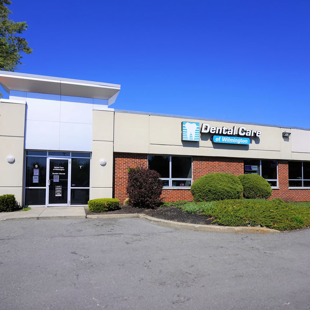 The image shows a dental care clinic with a sign indicating its name and services.