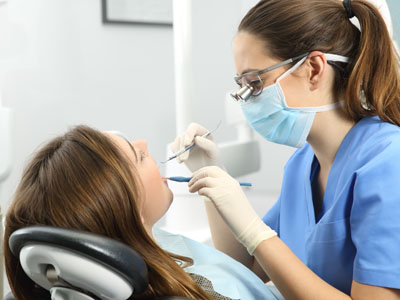A dental hygienist is performing a cleaning procedure on a patient's teeth, with the patient seated in a dental chair and wearing protective eyewear.