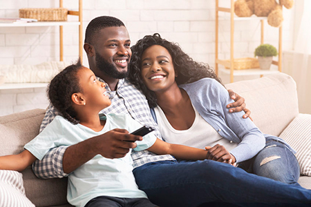 A family of four sitting together on a couch, smiling at the camera.